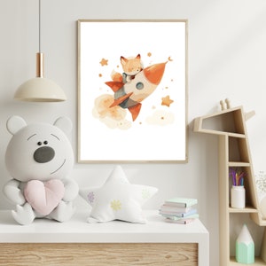 May include: A framed watercolor print depicts a fox in a space helmet riding a rocket ship through space. The rocket is orange and white, with a trail of orange smoke. Stars and a crescent moon are scattered around the rocket, creating a whimsical scene.