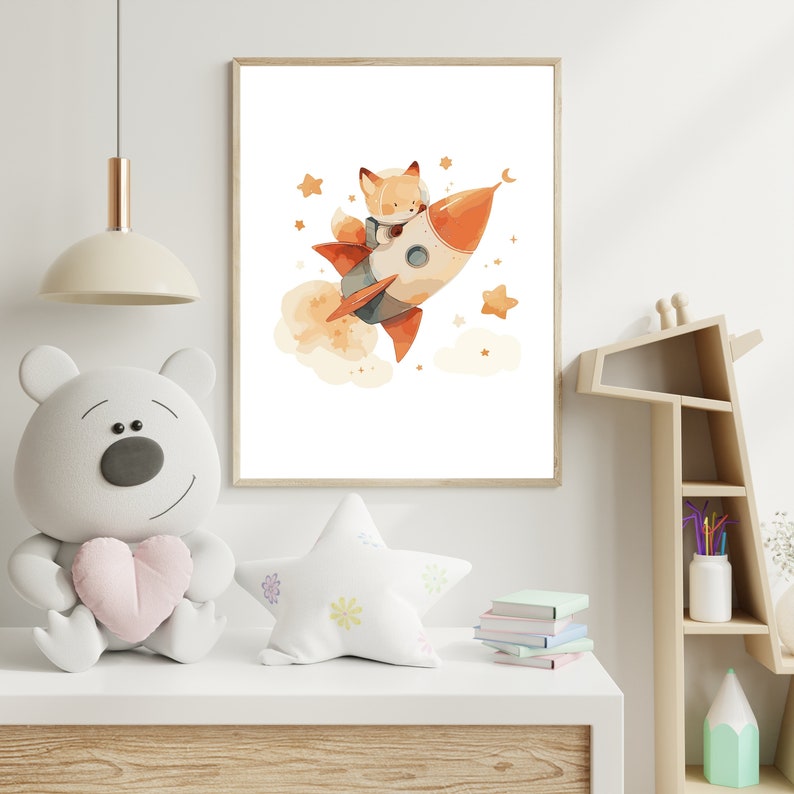 May include: A framed watercolor print depicts a fox in a space helmet riding a rocket ship through space. The rocket is orange and white, with a trail of orange smoke. Stars and a crescent moon are scattered around the rocket, creating a whimsical scene.
