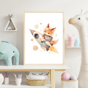 May include: A framed watercolor print featuring a cartoon fox in an astronaut suit riding a rocket ship through space. The artwork has a light color palette with orange, blue, and yellow accents, and is decorated with planets and stars. The print is displayed on a white shelf.