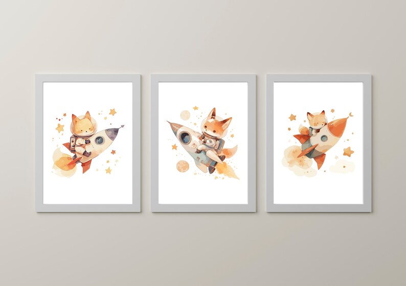 May include: Set of three framed watercolor prints featuring a fox astronaut in a rocket ship. The illustrations have a whimsical style with orange, white, and blue rockets, surrounded by stars and planets. The artwork is set against a white background.