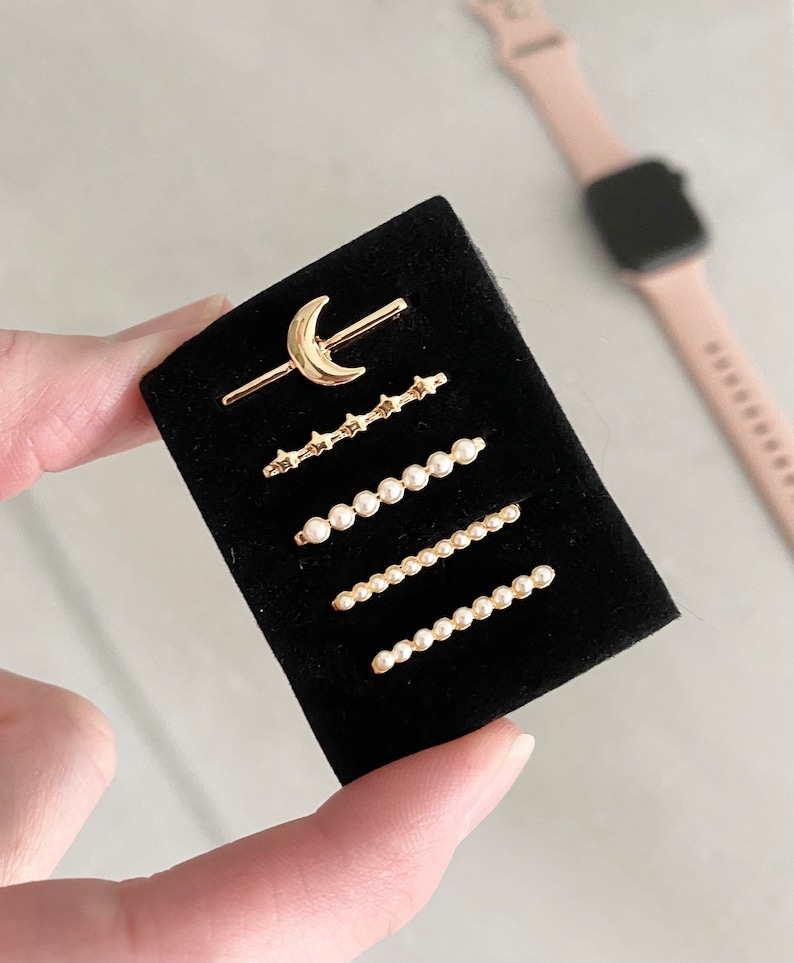 May include: A set of five gold-toned jewelry pieces on a black velvet background. The pieces include a crescent moon charm, a row of stars, and three rows of pearls.