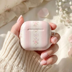 Könnte beinhalten: Eine rosa-weiß gestreifte AirPod-Hülle mit floralen Akzenten. Die Hülle hat ein vertikales Streifenmuster mit floralen Designs in Rosa, Lila und Grün. Sie hat eine kleine Schlaufe zum Befestigen an einem Schlüsselanhänger.