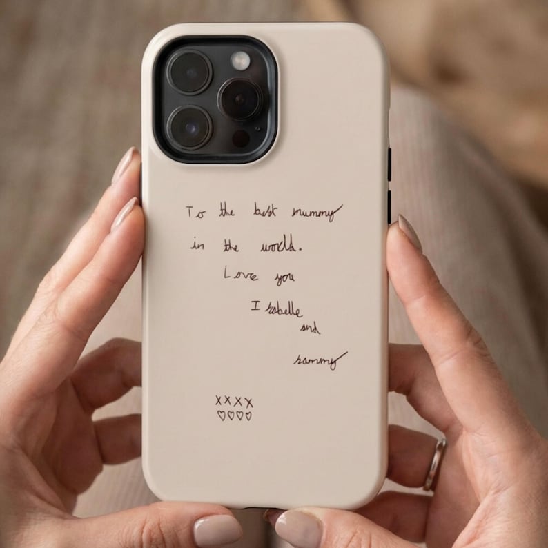 Może przedstawiać: Kremowe etui na smartfona z czarnym wycięciem na aparat i czarnym odręcznym tekstem: To the best mummy in the world. Love you I Isabelle and Sammy, zakończone czterema znakami X i czterema małymi symbolami serc u dołu obudowy.
