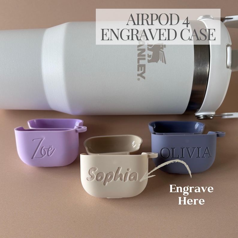 K&ouml;nnte beinhalten: Drei AirPod 4-H&uuml;llen aus Silikon in Helllila, Beige und Dunkelblau, jeweils mit einem individuell eingravierten Namen: Zoe, Sophia und OLIVIA. Dahinter steht ein wei&szlig;er Stanley-Becher mit dem Text AIRPOD 4 ENGRAVED CASE.