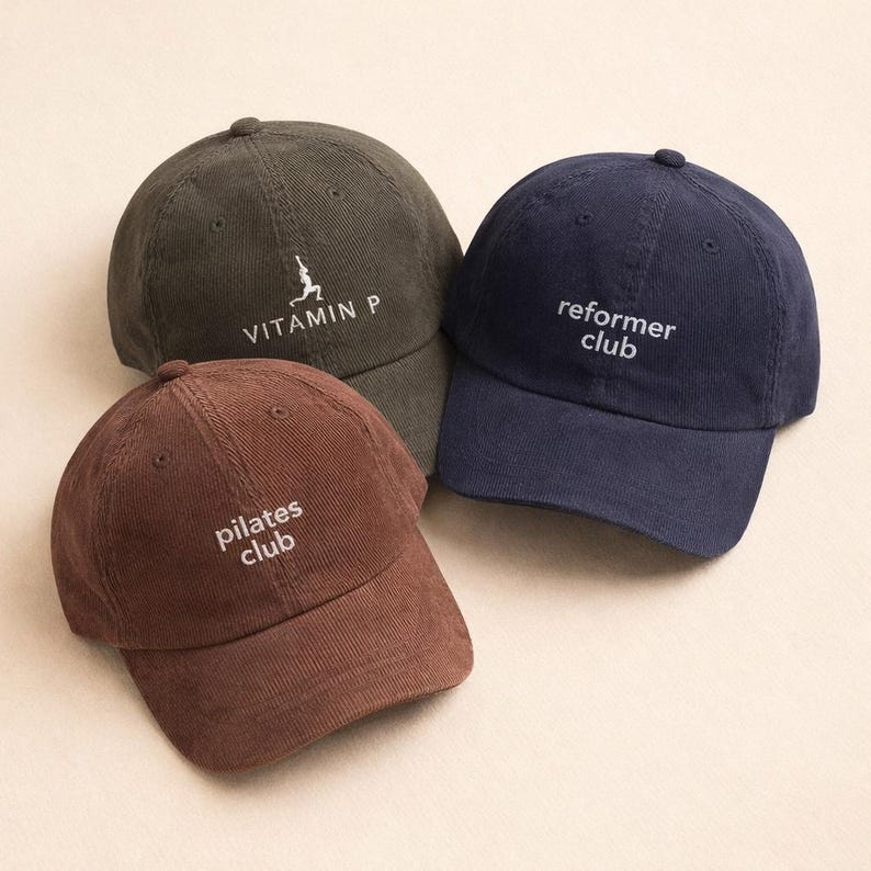 May include: Three corduroy baseball caps in olive green, navy blue, and brown. The olive green cap has the text "VITAMIN P" and a graphic. The navy blue cap has the text "reformer club". The brown cap has the text "pilates club".