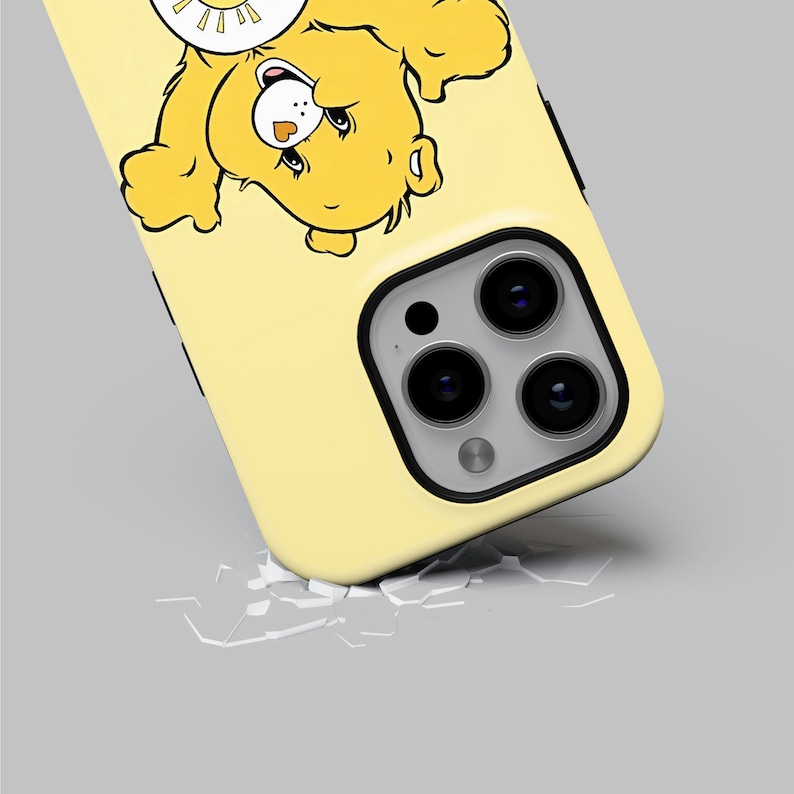 以下が含まれることがあります： 太陽の帽子をかぶった漫画のクマが描かれた黄色のiPhoneケース。ケースの背面にはカメラレンズの切り抜きがあります。