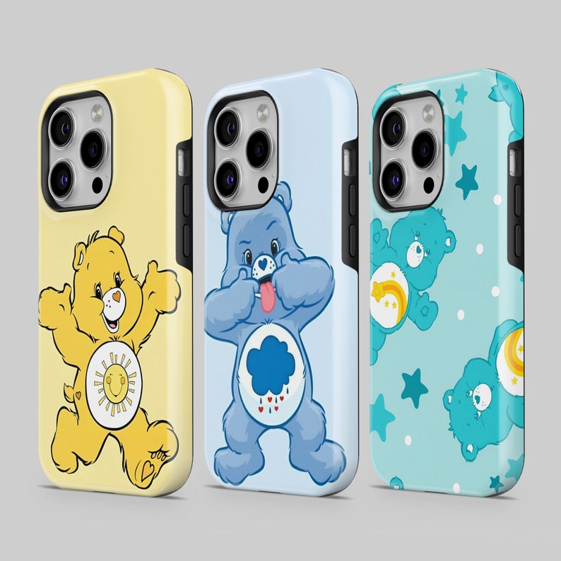 以下が含まれることがあります： 異なるケアベアのデザインが施された3つのiPhoneケース。最初のケースは、お腹に太陽が描かれたイエローのケアベア。2番目のケースは、お腹に雲と雨滴が描かれたブルーのケアベア。3番目のケースは、お腹に虹が描かれたブルーのケアベアです。