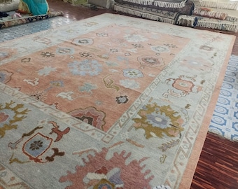 May include: A large rectangular area rug featuring a central peach-colored field with scattered floral and geometric motifs in blue, brown, and cream. The rug has a wide light gray border with intricate patterns and the text ABSCARPET.