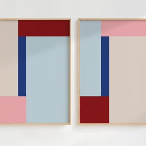 May include: Two framed abstract art prints. Each print features a geometric design with blocks of colour including light blue, pink, beige, navy, and burgundy. The frames are a light wood colour.