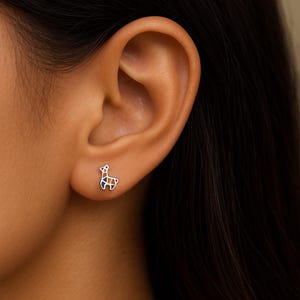 Könnte beinhalten: Ein silberner Llama-Ohrstecker mit geometrischem Design. Das Lama ist mit orangefarbenen, blauen und grünen Segmenten gefüllt. Der Ohrring wird am Ohr einer Person gezeigt.