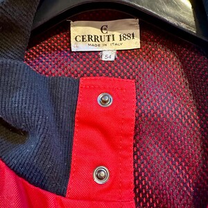 Puede incluir: Primer plano de una chaqueta roja y azul marino con la etiqueta "CERRUTI 1881 MADE IN ITALY". La chaqueta tiene un forro de malla y dos cierres de presi&oacute;n plateados. La etiqueta de talla dice "54".