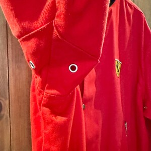 Puede incluir: Chaqueta roja brillante con cuello y pu&ntilde;os negros. La chaqueta presenta un emblema dorado en el pecho y cierre de botones. El pu&ntilde;o de la manga tiene un ojal. La chaqueta es de material suave.