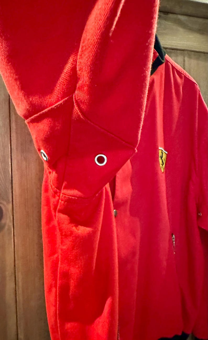 Puede incluir: Chaqueta roja brillante con cuello y pu&ntilde;os negros. La chaqueta presenta un emblema dorado en el pecho y cierre de botones. El pu&ntilde;o de la manga tiene un ojal. La chaqueta es de material suave.