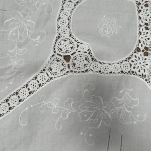 May include: White cotton tablecloth with delicate crocheted lace trim and embroidered floral designs.