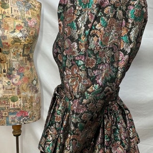 Puede incluir: Un vestido de brocado negro, dorado y verde con una falda con volantes y una cintura ce&ntilde;ida.