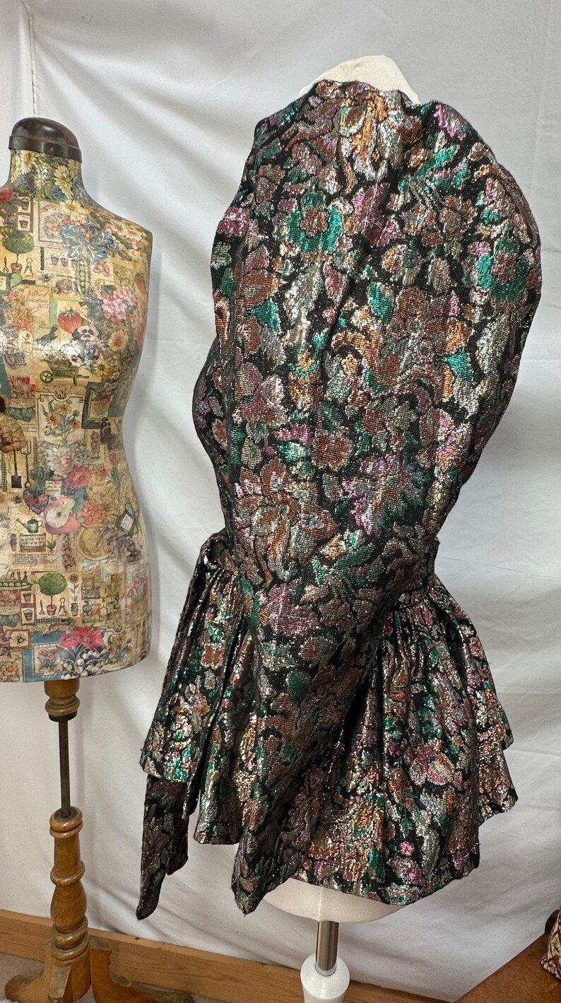 Puede incluir: Un vestido de brocado negro, dorado y verde con una falda con volantes y una cintura ce&ntilde;ida.