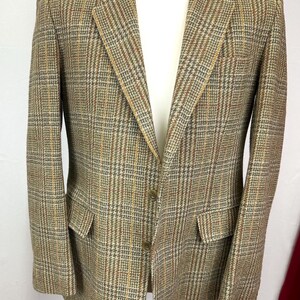 Puede incluir: Una chaqueta de traje de cuadros marrones, beige y naranja con un cierre de botón.