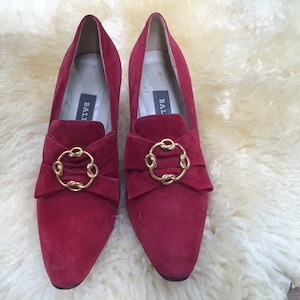 Puede incluir: Un par de zapatos de ante rojo con adornos de cadena dorada y la palabra "BALLI" escrita en el interior de cada zapato.