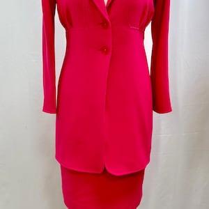 Könnte beinhalten: Ein pinkfarbener Anzug mit Jacke und Rock mit einem einzigen Knopfverschluss. Die Jacke hat lange Ärmel und einen V-Ausschnitt.