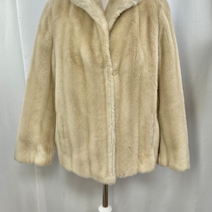 Puede incluir: Una chaqueta de piel sintética de color crema con cuello y cierre de cremallera.