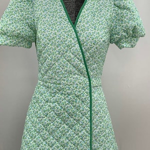 May include: A white dress with a green floral print and green trim. The dress has a V-neckline and short puffed sleeves.