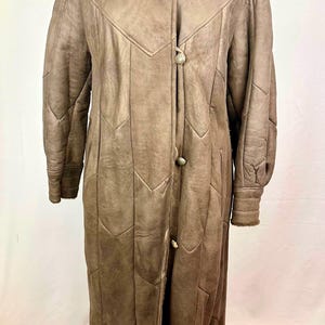 May include: A long brown leather coat with a fur collar and button closures. The coat has a quilted design and is made of sheepskin.