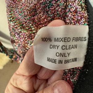 Puede incluir: Primer plano de una etiqueta de tela blanca con texto negro que dice "100% Fibras Mixtas Limpieza en Seco Solo Hecho en Gran Breta&ntilde;a".