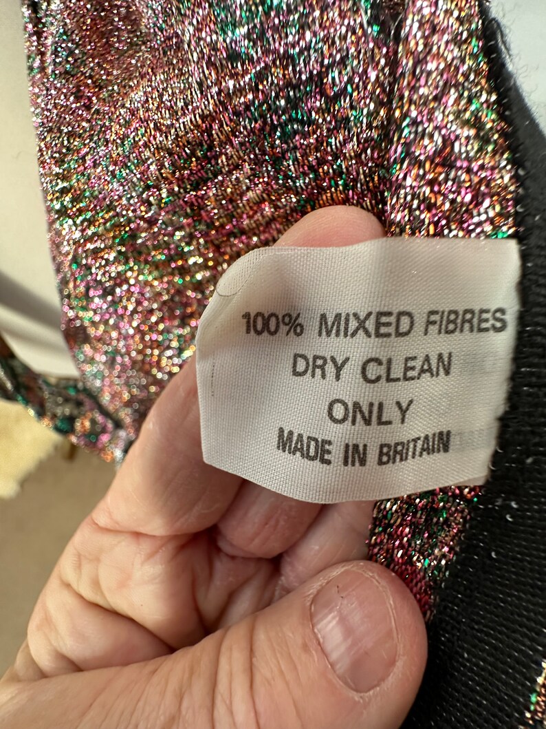 Puede incluir: Primer plano de una etiqueta de tela blanca con texto negro que dice "100% Fibras Mixtas Limpieza en Seco Solo Hecho en Gran Breta&ntilde;a".