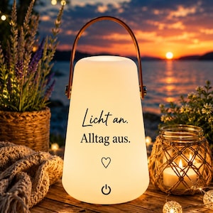 Könnte beinhalten: Eine tragbare, kegelförmige LED-Laterne mit mattweißer Oberfläche und einem braunen Griff. Auf der Vorderseite befindet sich der schwarze Text "Licht an. Alltag aus." über einem Herzsymbol und einem Power-Button-Symbol.