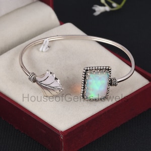 Puede incluir: Un brazalete de plata con un diseño de hoja en un extremo y una piedra de ópalo cuadrada engastada en un marco de plata en el otro extremo.