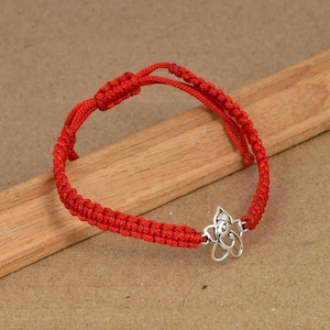 Peut inclure: Un bracelet en cordon rouge doté d'une breloque en métal argenté représentant la tête d'une divinité éléphant. Le bracelet est fabriqué à partir d'un cordon rouge tressé et comprend un mécanisme de fermeture à nœud coulissant réglable.
