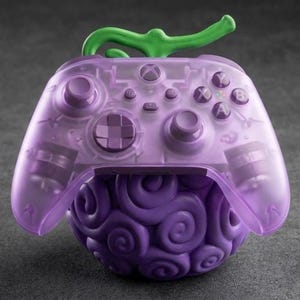 Puede incluir: Un mando de Xbox morado con un diseño único, con un cuerpo translúcido y una base estilizada y arremolinada. El mando tiene detalles verdes y está sobre un fondo gris.