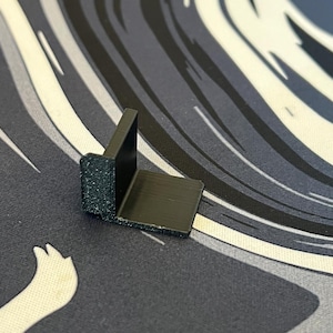 Puede incluir: Un ángulo de esquina de plástico negro, diseñado para reforzar y soportar esquinas en varios proyectos.