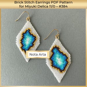 May include: A pair of white and blue beaded earrings with a gold hook. The earrings are in the shape of a diamond and feature a blue and white geometric pattern. The earrings are labelled "Nota Arta".