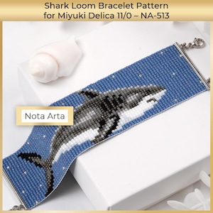Könnte beinhalten: Ein Perlenarmband mit einem Hai-Design. Das Armband ist hauptsächlich blau und zeigt ein detailliertes Hai-Bild in Grau- und Weißtönen. Der Text "Nota Arta" ist sichtbar. Das Armband wird mit silbernen Verschlüssen befestigt.