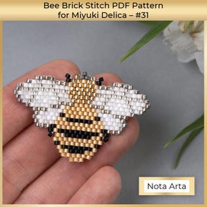 Puede incluir: Una abeja de cuentas con cuentas negras, doradas y blancas. La abeja tiene alas y está hecha con la técnica de punto de ladrillo. La abeja está sostenida en una mano. La imagen incluye el texto "Nota Arta".