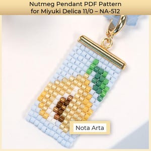 May include: A beaded pendant featuring a nutmeg design, crafted with Miyuki Delica beads. The pendant has a light blue background with a gold-colored metal clasp and a small tag that reads "Nota Arta". The text "Nutmeg Pendant PDF Pattern" is at the top.