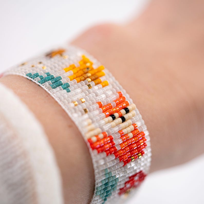 Puede incluir: Una pulsera de cuentas con fondo blanco, con patrones coloridos en naranja, amarillo, turquesa y negro. La pulsera est&aacute; hecha de peque&ntilde;as cuentas de colores y se lleva en la mu&ntilde;eca.