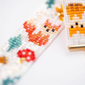 Puede incluir: Primer plano de una pulsera de cuentas con tem&aacute;tica de bosque. La pulsera presenta un fondo blanco con zorros naranjas, setas rojas y &aacute;rboles verde azulado. Las cuentas son peque&ntilde;as y coloridas, creando un dise&ntilde;o detallado. La pulsera tiene un cierre dorado.