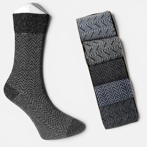 May include: A single grey herringbone sock on a white background, alongside a box of folded socks in shades of grey and navy. The socks feature a dark grey cuff and heel. The folded socks have a similar pattern.