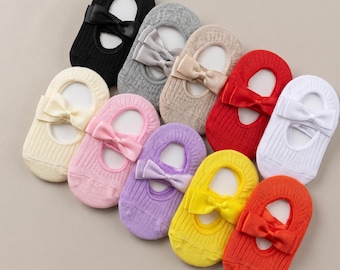 May include: A collection of ten low-cut, ribbed ankle socks arranged in a circular pattern. Each sock features a solid color, including black, gray, beige, red, white, pink, purple, yellow, and orange, and is adorned with a matching satin bow.