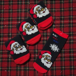 May include: Four black Christmas socks with red toes and cuffs. Each sock features a Santa Claus face with a red hat and white beard. One sock has the words "HO! HO! HO!" and a snowflake design.