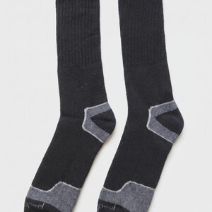 May include: A pair of black crew-length socks featuring ribbed cuffs and grey reinforced panels at the heels and toes. The toe area of each sock displays the word "peal" in small, light-colored lettering, indicating the brand name on the fabric.