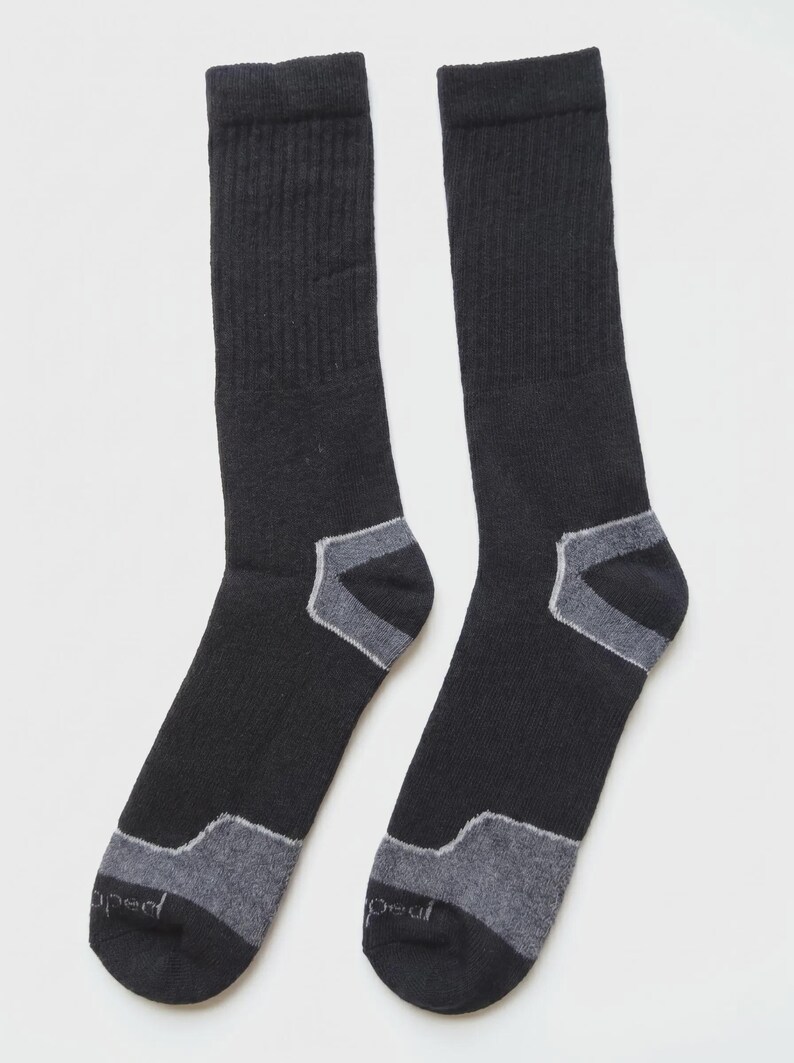 May include: A pair of black crew-length socks featuring ribbed cuffs and grey reinforced panels at the heels and toes. The toe area of each sock displays the word "peal" in small, light-colored lettering, indicating the brand name on the fabric.