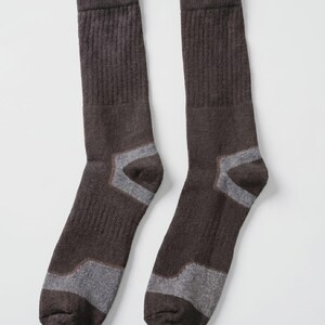 May include: A pair of dark brown crew socks featuring a ribbed texture on the upper leg section and contrasting light gray panels at the heel and toe areas. The socks are constructed with a knit fabric and have a standard mid-calf length design.