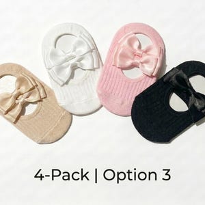 Four baby knit hats with large satin bows in beige, white, pink, and black arranged in a curved row on a white background.