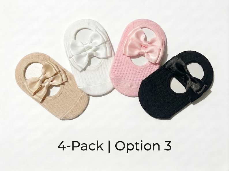 Four baby knit hats with large satin bows in beige, white, pink, and black arranged in a curved row on a white background.