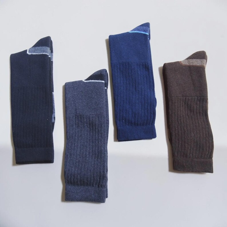 May include: Four pairs of crew socks in various colors including dark navy, heathered blue, royal blue, and dark brown. Each sock features a ribbed texture along the leg and a contrasting color block detail at the heel and toe area for a distinct look.