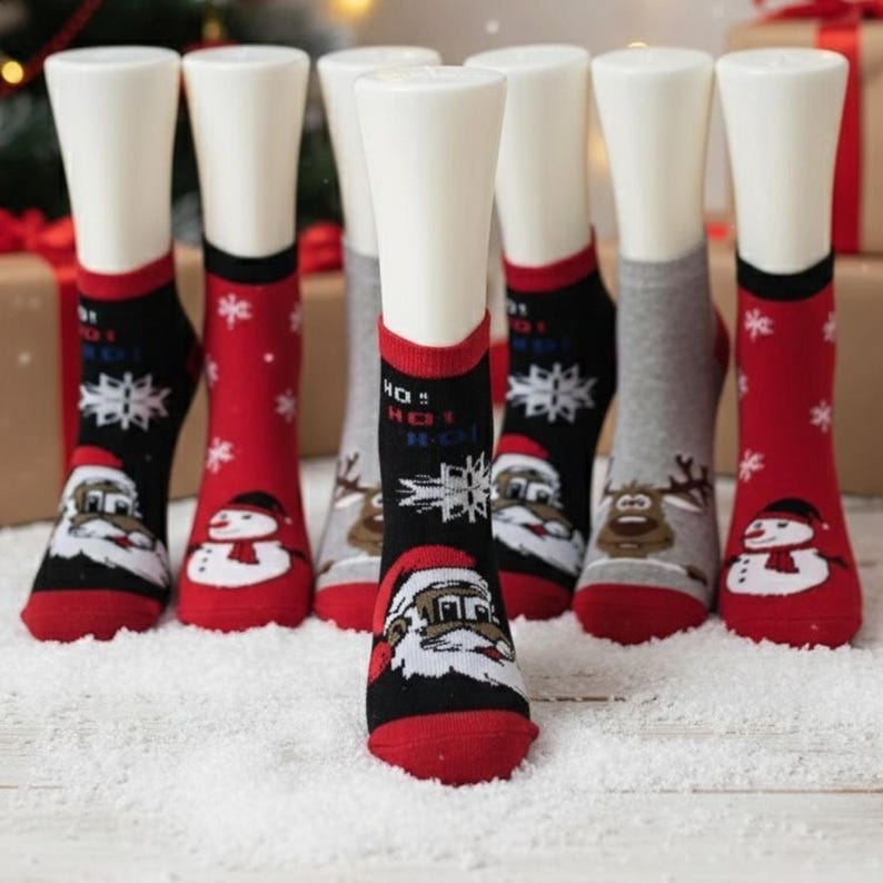 Colorful Christmas-themed socks with Santa, snowman, snowflake, and reindeer designs displayed on white mannequin legs, set on artificial snow in front of holiday gift boxes and a decorated Christmas tree.