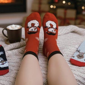 Cozy winter scene with christmas festive socks featuring snowmen, Santa, and a reindeer, alongside a hot chocolate in a mug by a warm fireplace.